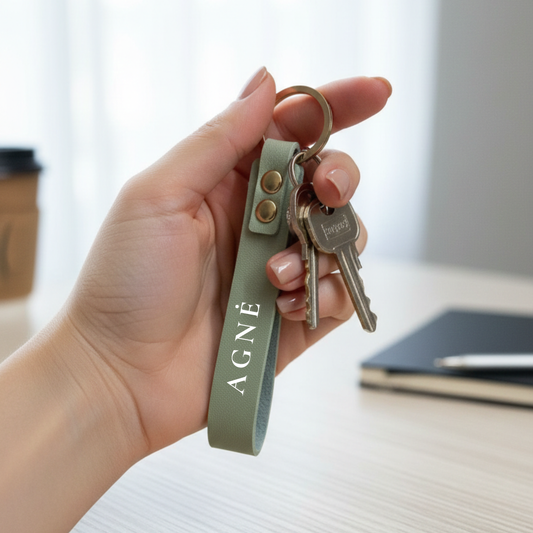 Rankoje laikomas juodas odinis rakto pakabukas su metaliniu žiedu ir raktų ryšuliu – minimalistinis aksesuaras el. parduotuvei