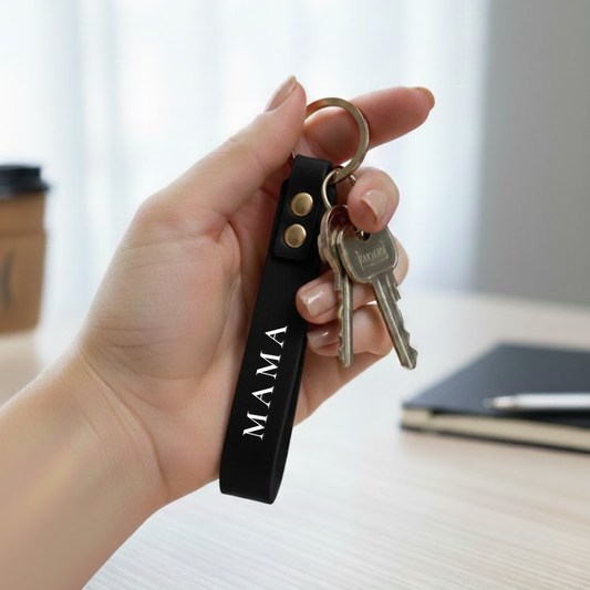 Rankoje laikomas juodas odinis rakto pakabukas su metaliniu žiedu ir raktų ryšuliu – minimalistinis aksesuaras el. parduotuvei